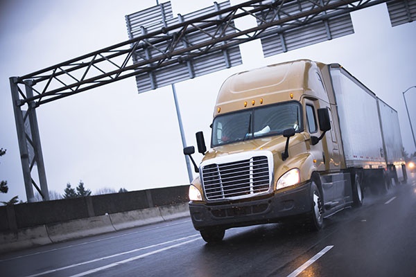 Brown modern big rig semi truck popular among drivers truckers going to long haul commercial cargo  driving on a wet road in the rain with headlights for safe driving and reflection of lights.