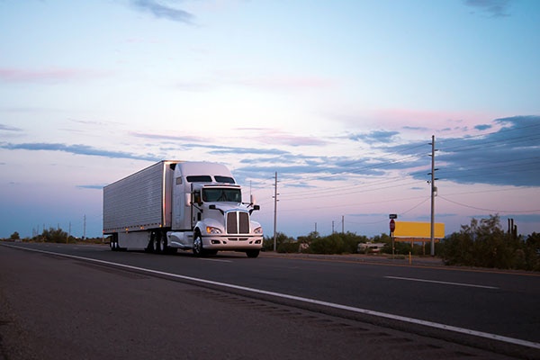The most popular model in the American big rig semi truck with a reefer trailer moving with cargo on the evening highway road in Arizona reflecting the last rays of the setting sun