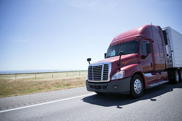 A large, powerful modern semi truck with a reefer unit and refrigerated trailer carries perishable cargoes that require storage at low temperatures along the direct roads of sunny California